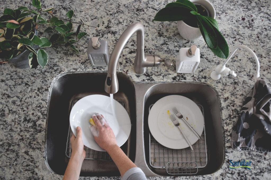 Person comfortably washing dishes at a clean kitchen sink with a Sanitar mixer faucet