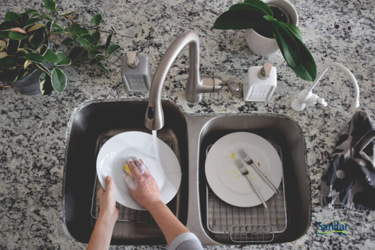 Person comfortably washing dishes at a clean kitchen sink with a Sanitar mixer faucet