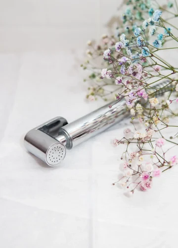 Hygiene and cleanliness concept. New hygienic chrome-plated shower in hand against a background of white tiles. Bathroom